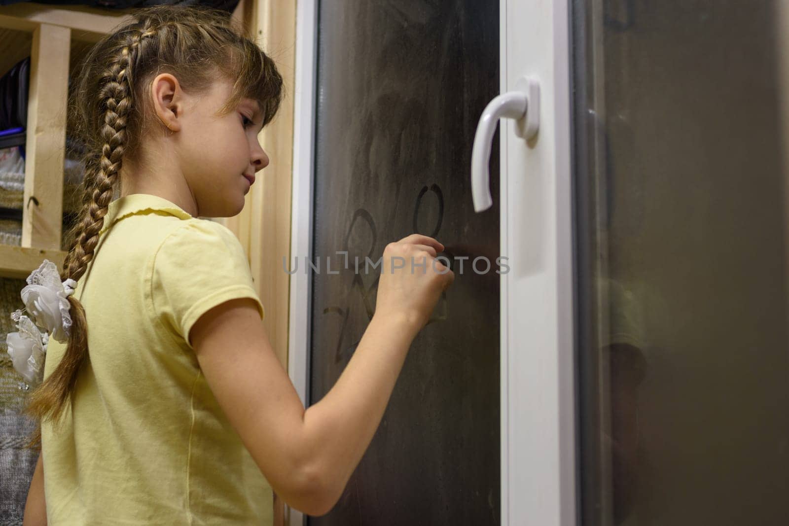 Girl draws figures of little men on a fogged window
