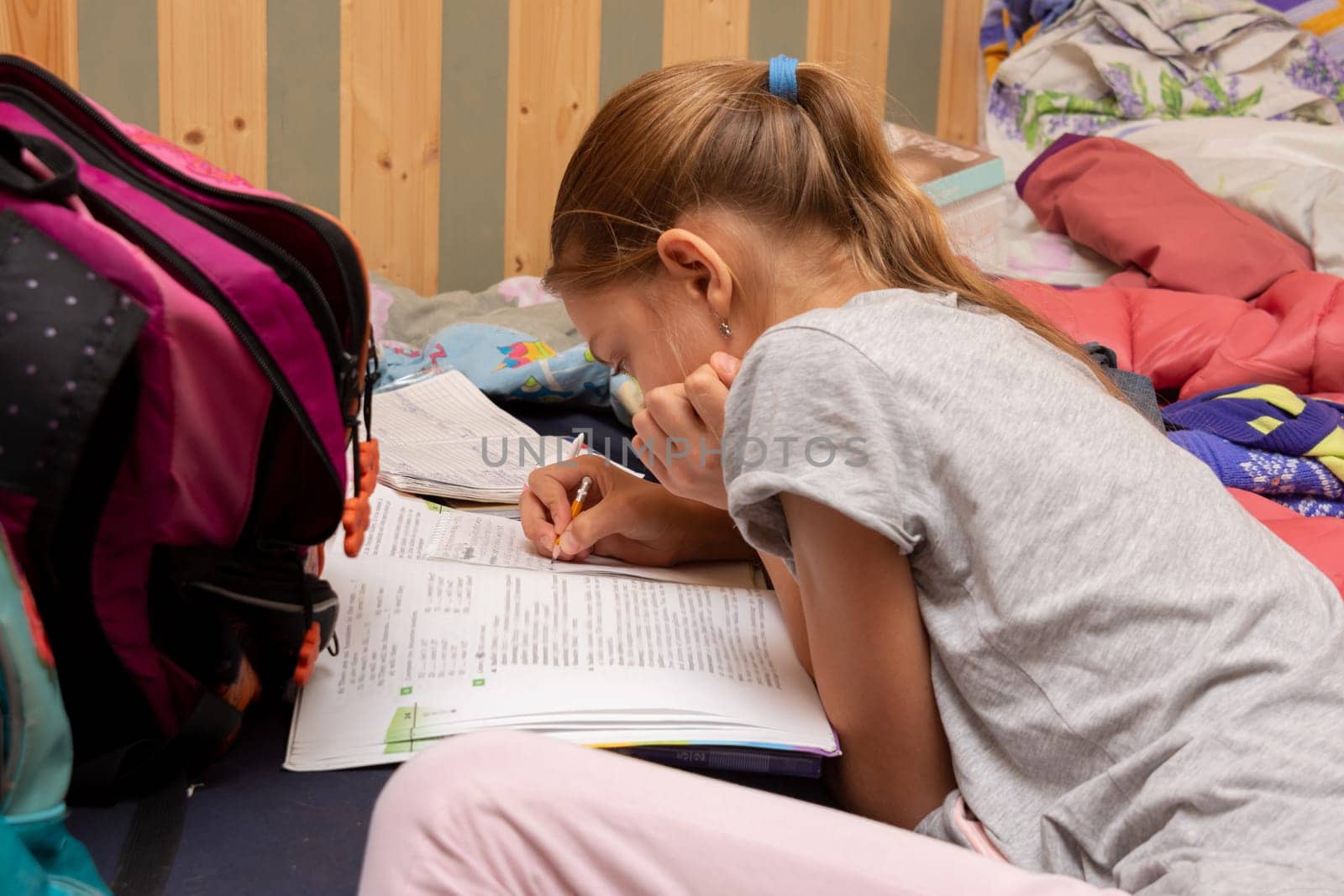 Schoolgirl does her homework on a spread out couch piled high with things
