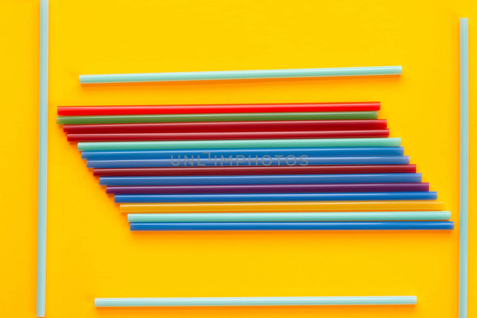 A bunch of multicolored cocktail tubes lies on a yellow background