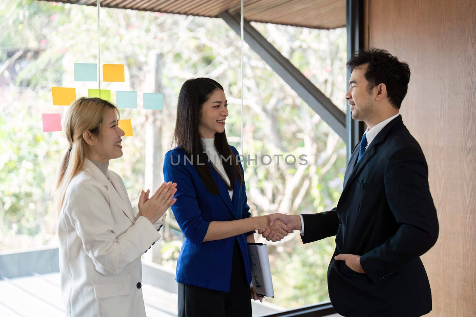 A diverse business team celebrates a successful partnership with a handshake in a bright, contemporary office setting.