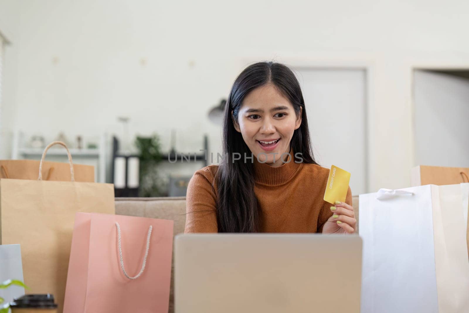 A smiling woman holds her credit card while shopping online, celebrating her successful purchase with excitement.