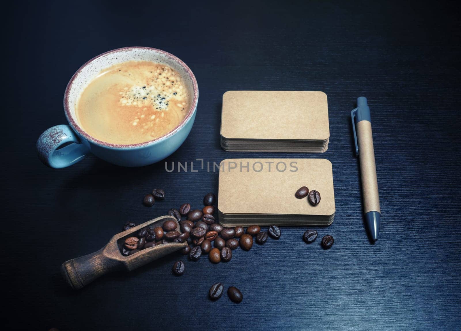 Photo of blank kraft business cards, coffee cup, coffee beans and pen on black wooden background. Responsive design mockup.