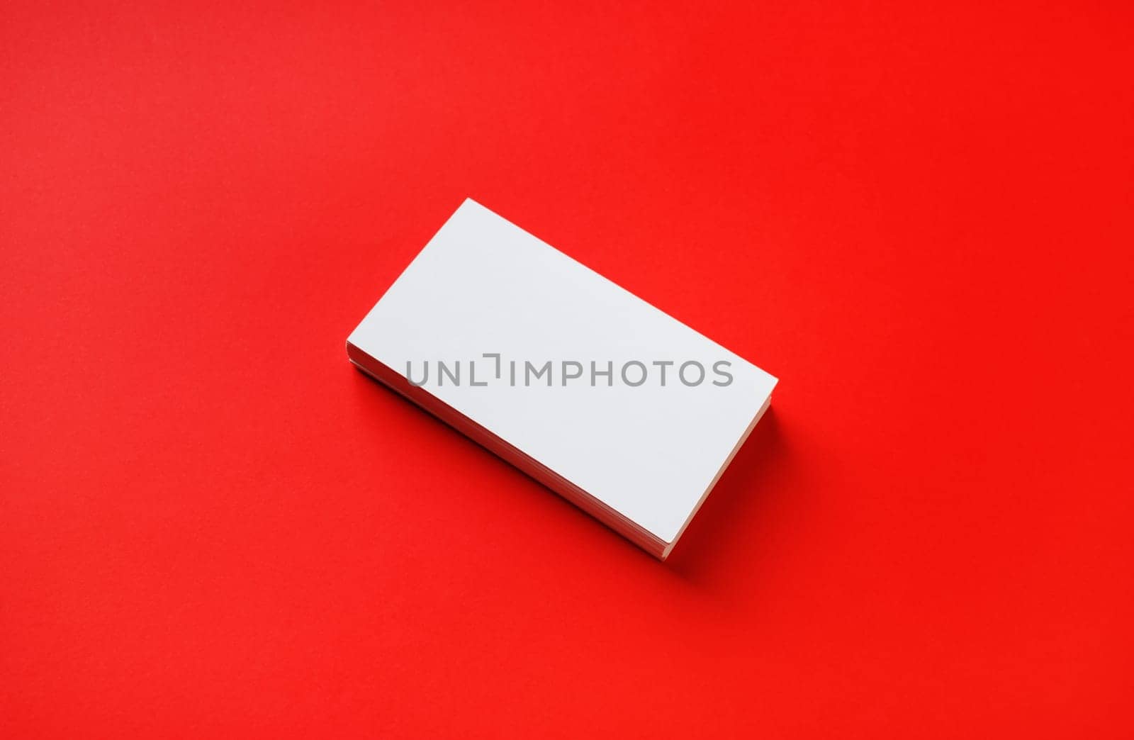 Photo of blank business card on red paper background. Mock-up for branding identity.