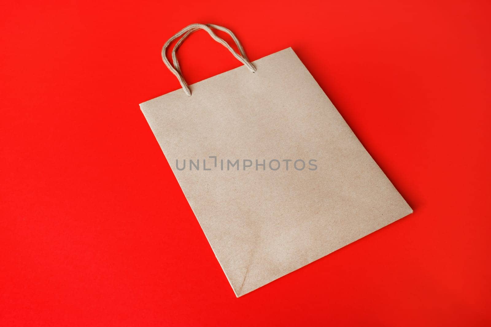 Blank kraft paper bag on red paper background. Recyclable package. Template ready for your design.
