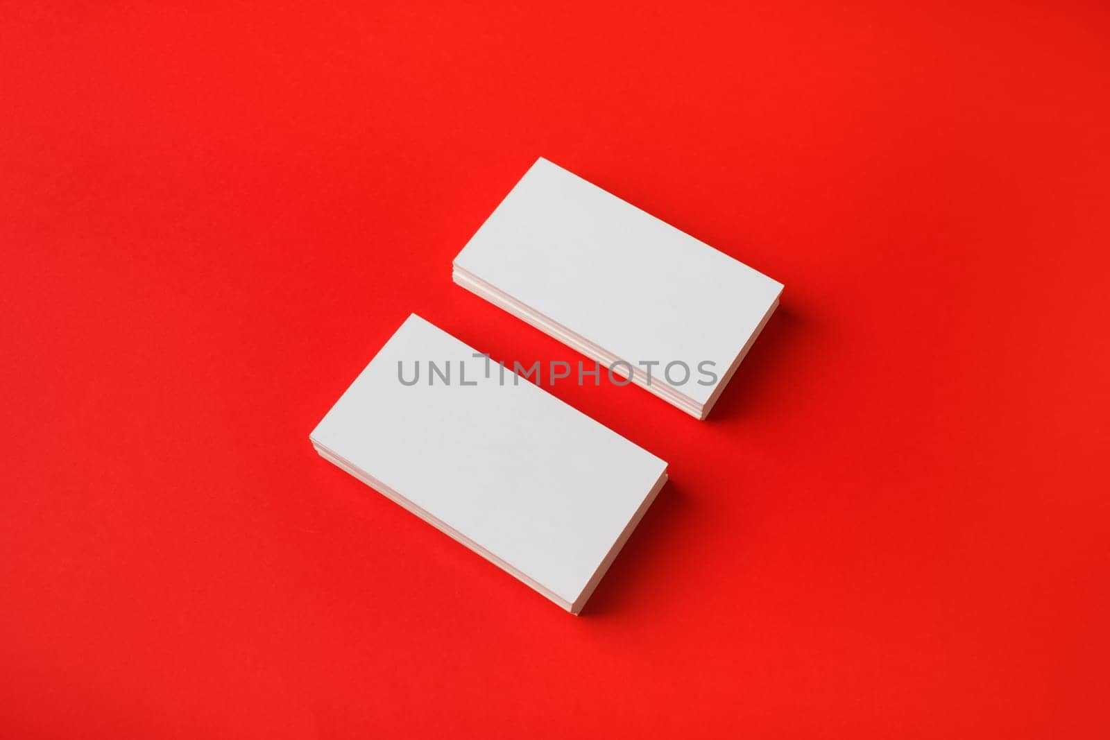Two blank business cards on red paper background. Branding mockup.