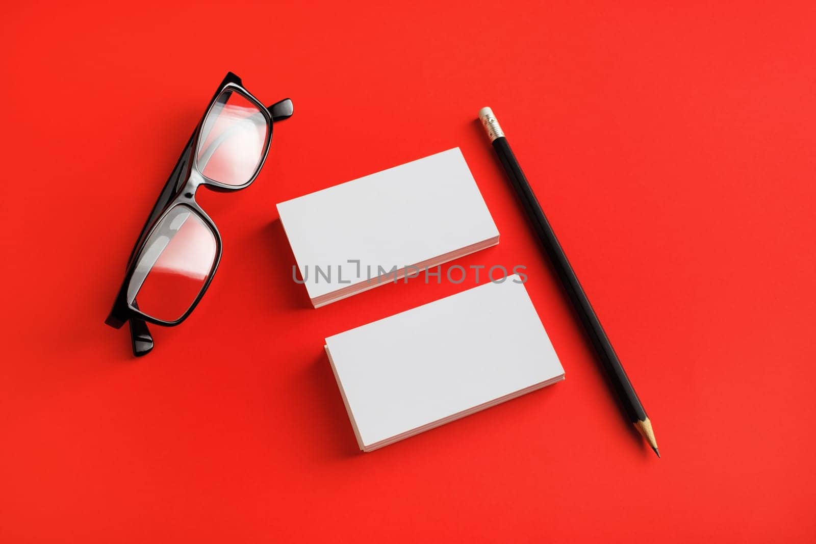 Photo of blank stationery set. Business cards, glasses and pencil on red paper background. Template for placing your design.