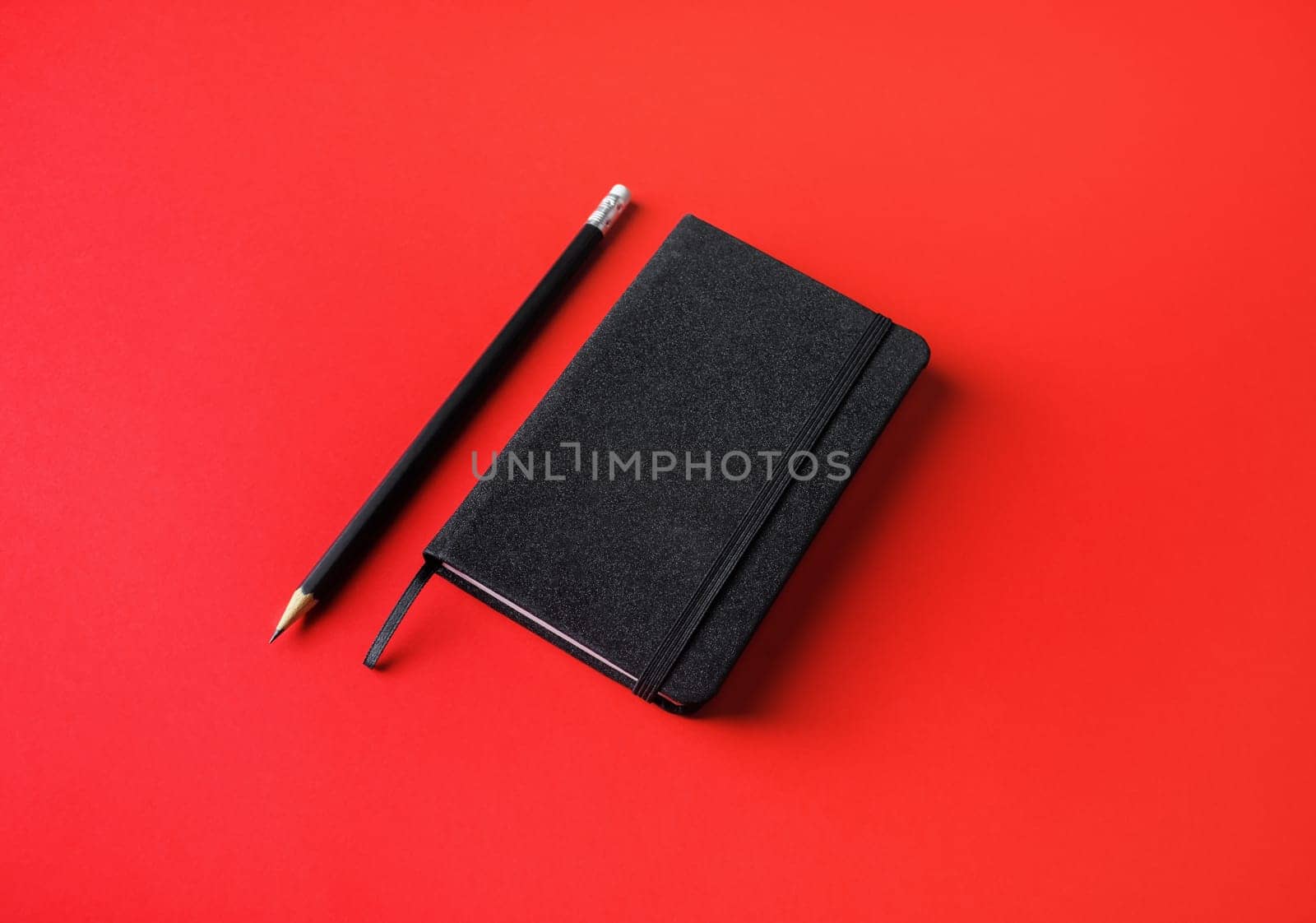 Blank black notebook and pencil on red paper background.