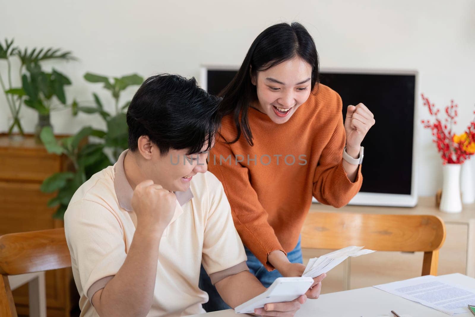 A joyful couple celebrates their financial planning success while reviewing bills and using a calculator at home.