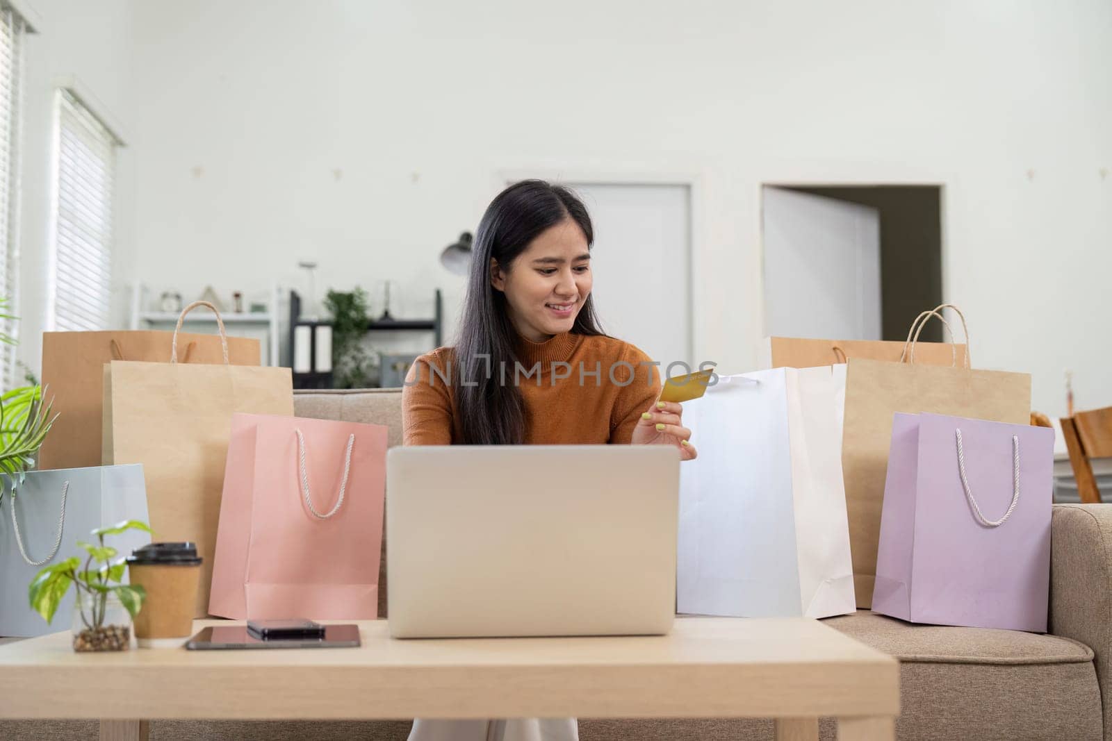 A joyful woman shops online with her credit card, surrounded by shopping bags, expressing excitement over her purchase.