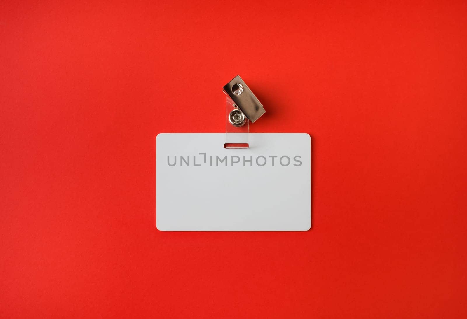 Photo of blank white plastic badge on red paper background. Blank id card. Top view. Flat lay.