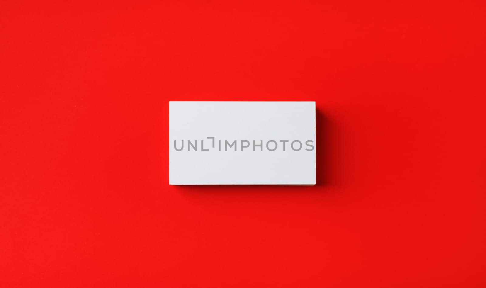Photo of blank business card on red paper background. Template for branding identity. Mockup for ID. Flat lay.