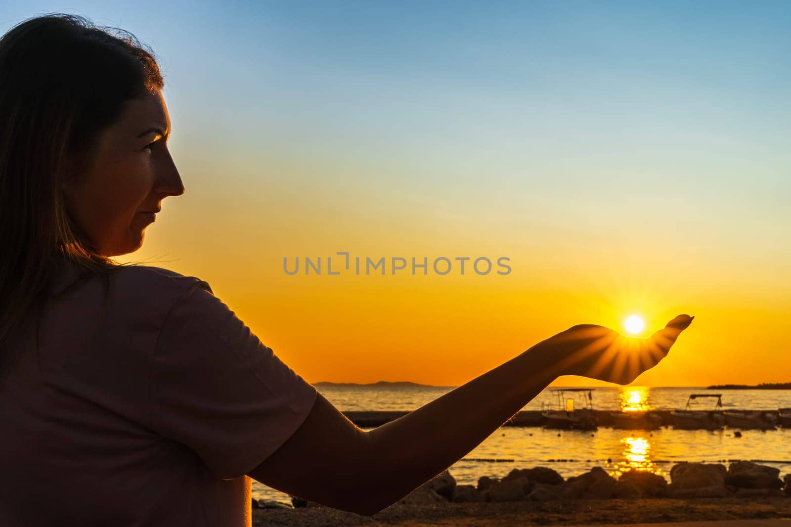 Beautiful woman holding sun in her hand or palm, witch trough shines Sunstar with sunrays at beautiful sunset on beach at Adriatic Sea, Zaton, Croatia