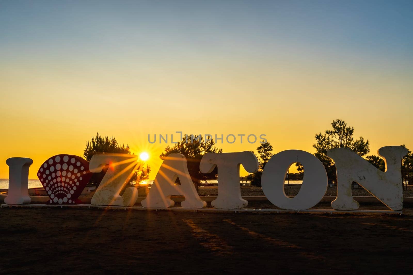 Amazing sunset and silhouette of I Love Zaton text, a welcome sign on the beach at Adriatic Sea with defined Sunstar between letters, Croatia