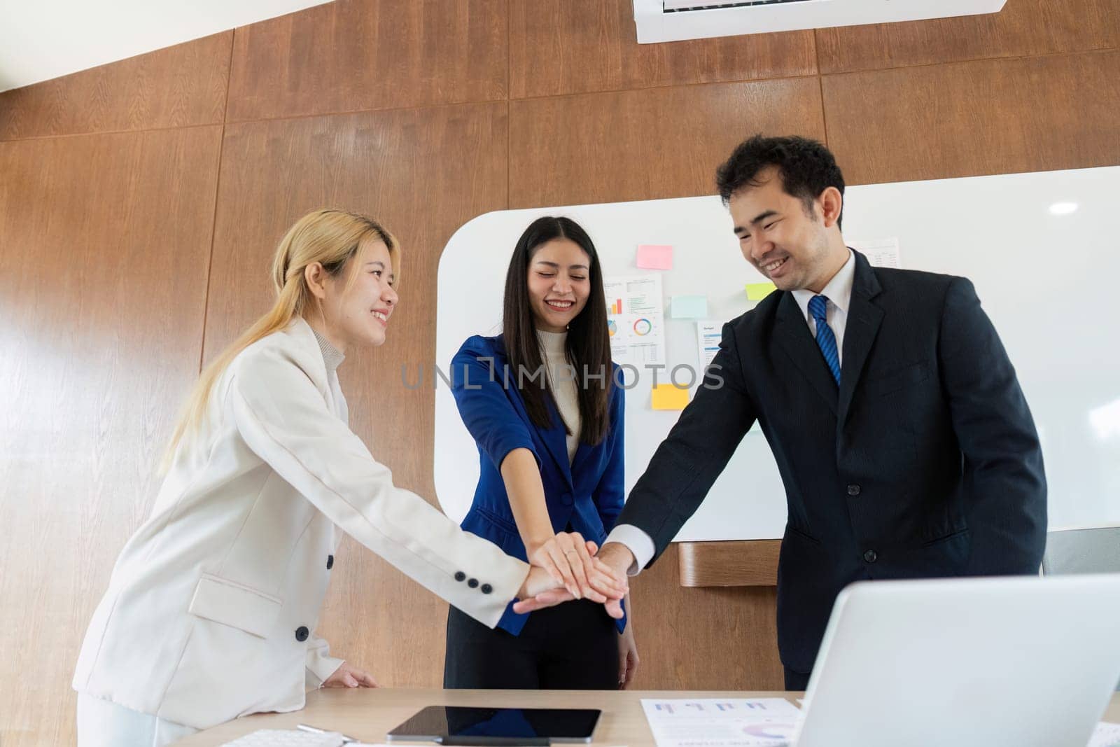 A diverse business team celebrates their success with a group huddle, showcasing teamwork and camaraderie in a modern office.