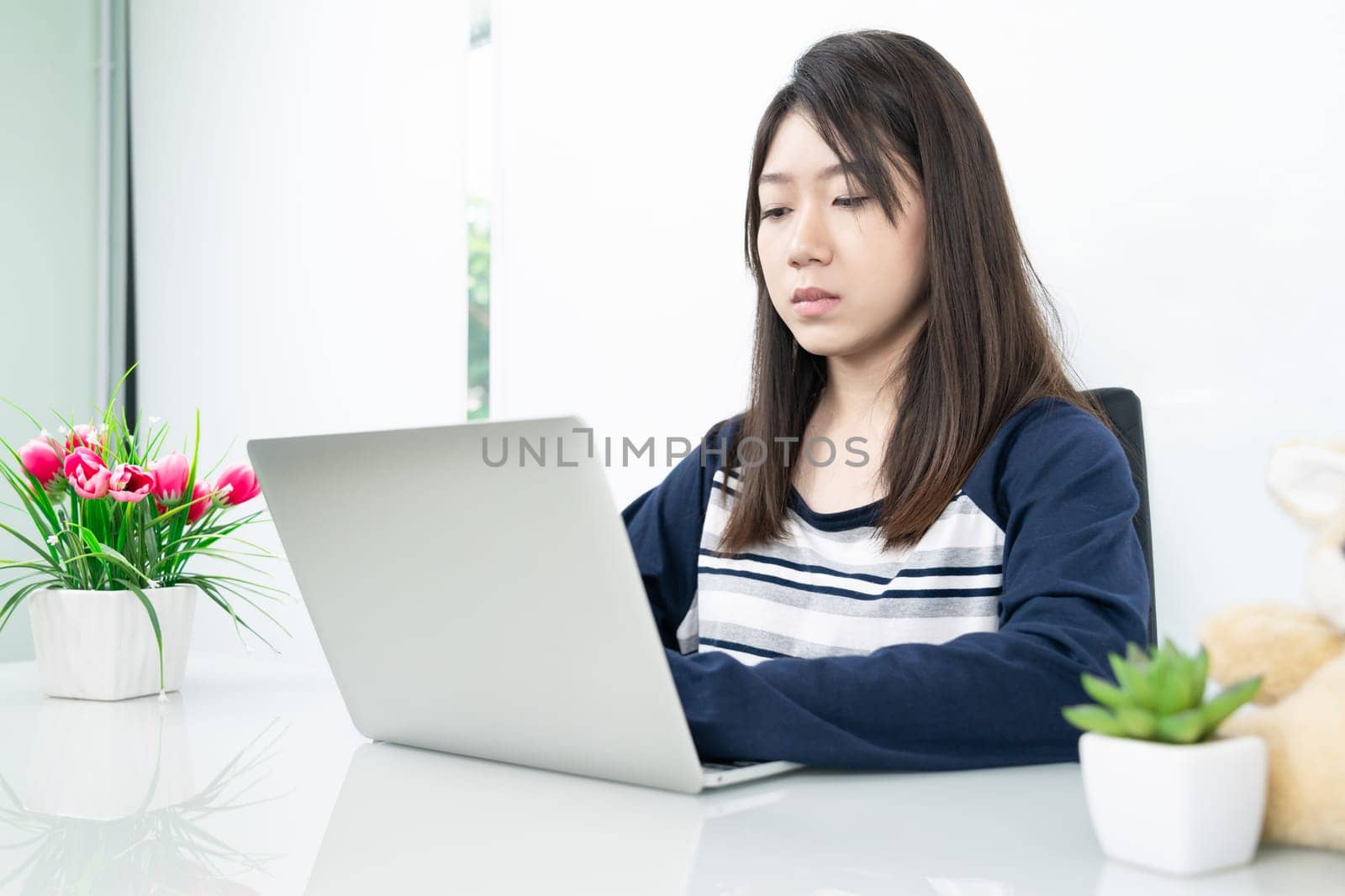 Young female student sitting in living room using laptop at desk learning online