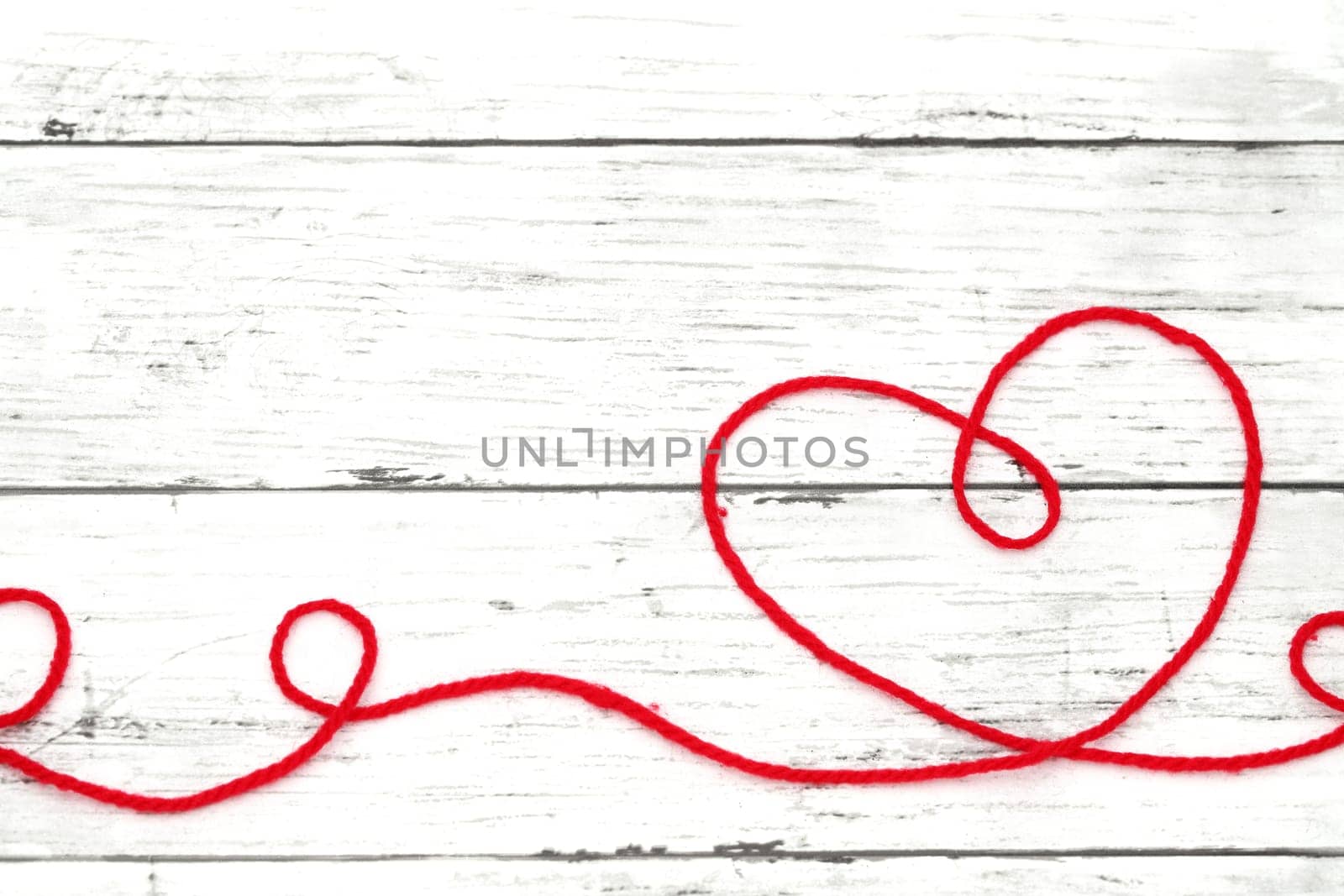 Red woolen thread in the shape of heart on white wooden table　