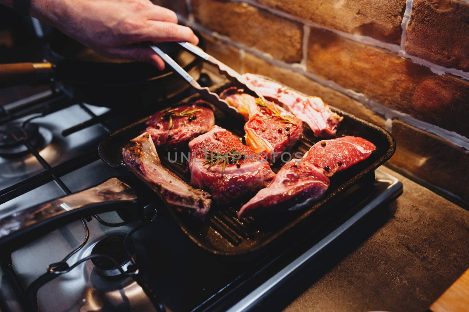 Hand turns steak with tongs during preparation on the grill pan with seasonings. High quality photo