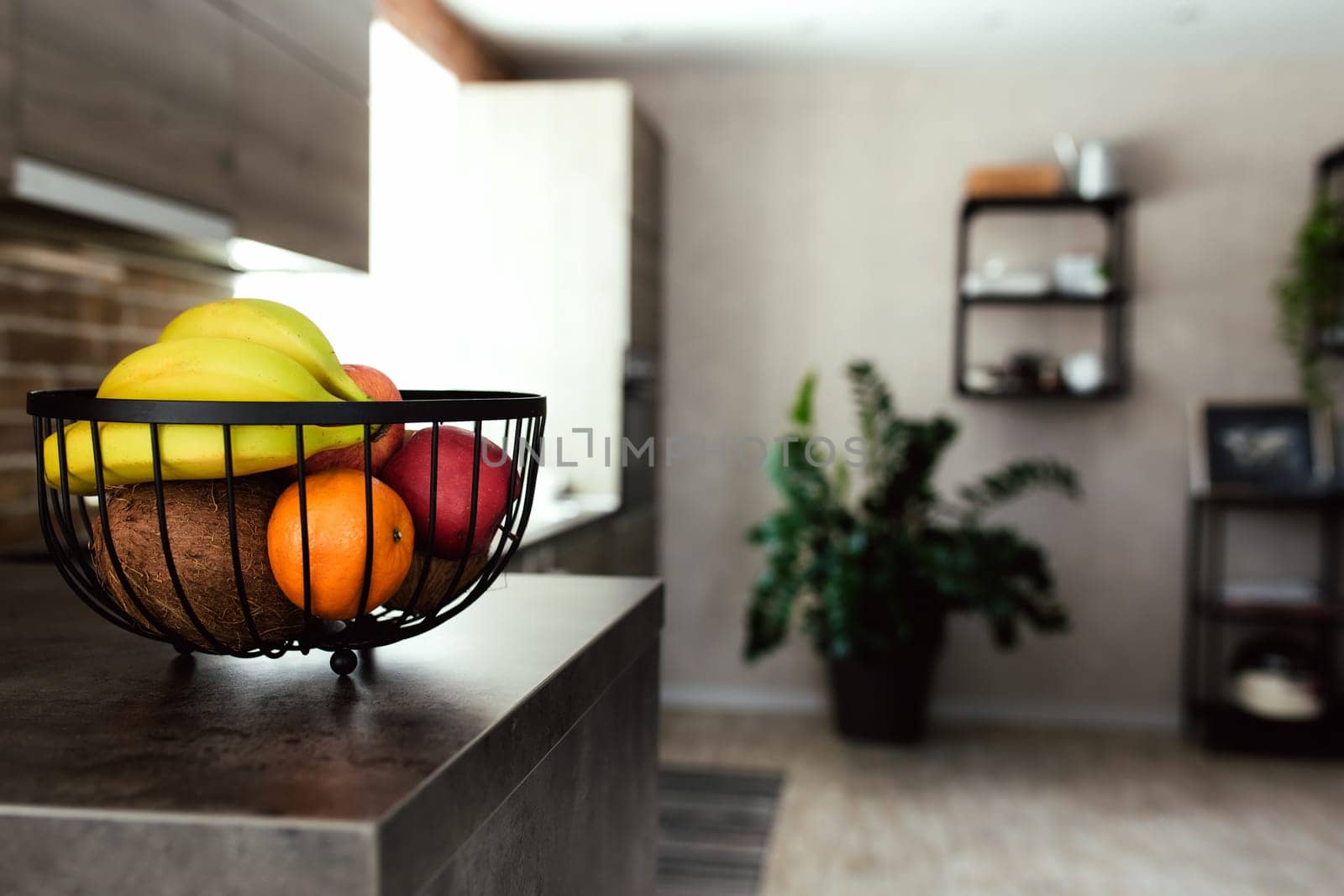 Tropical fruits: broken coconut, apple, tangerine, orange, banana in fruit bowl on bar counter in stylish loft kitchen. Blurred background. High quality photo