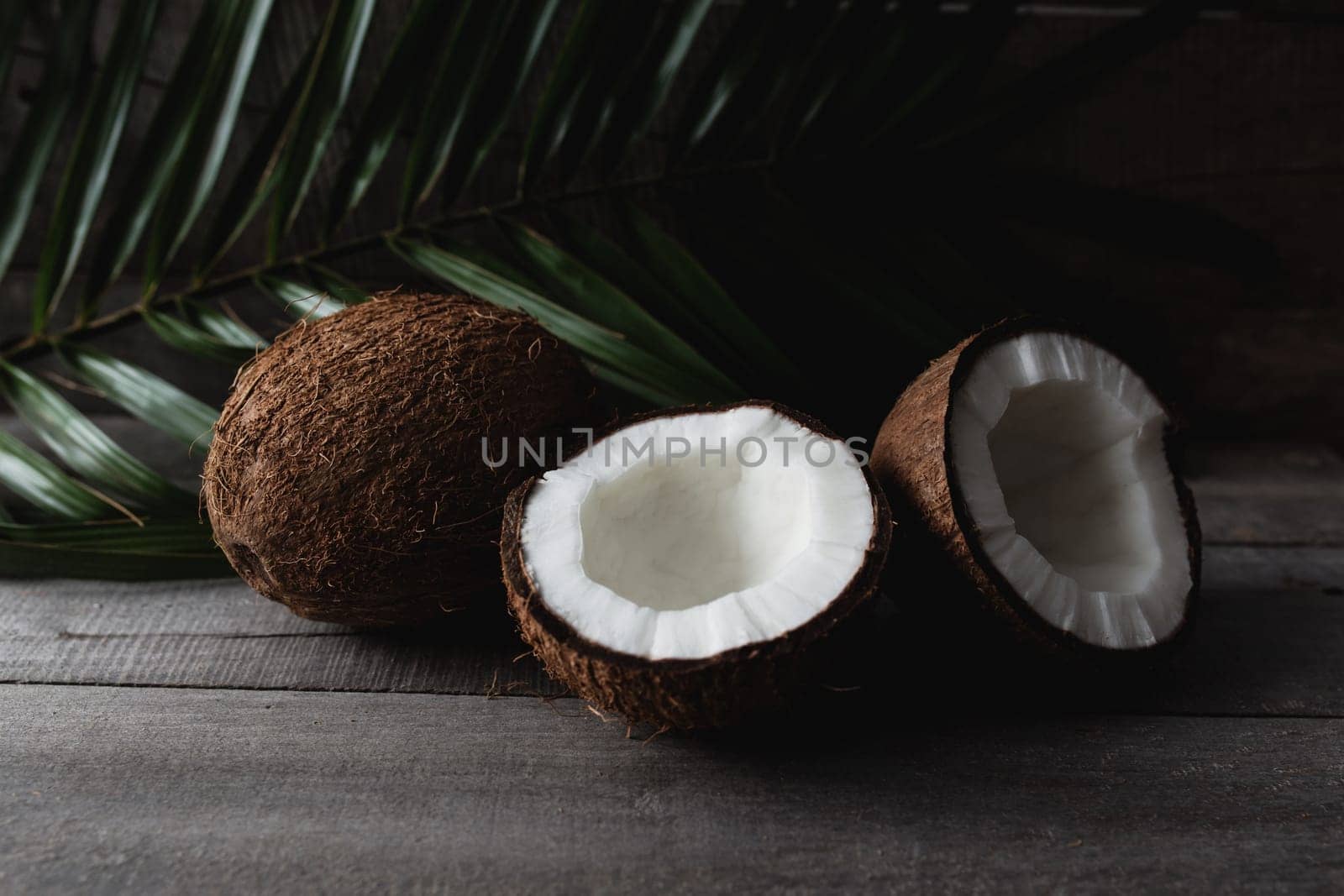 Broken coconuts on gray wooden background with palm leaf. White coconut pulp. High quality photo