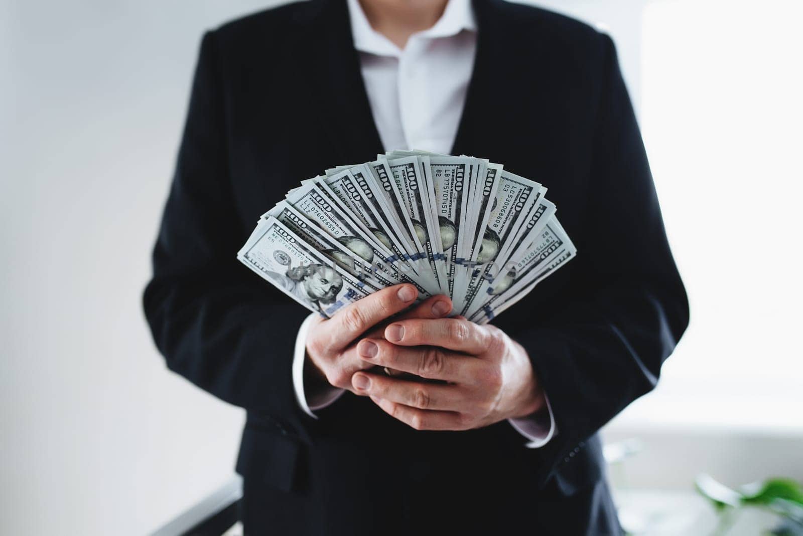 One hundred dollar bills money fun, in hand of man in suit and white shirt. Blurred background. High quality photo