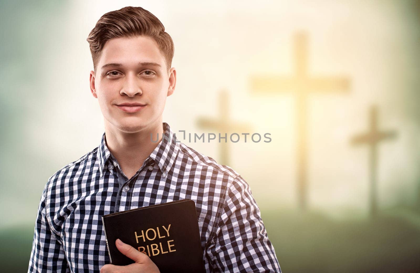Young handsome happy man holding a Bible with tree crosses background (easter concept)