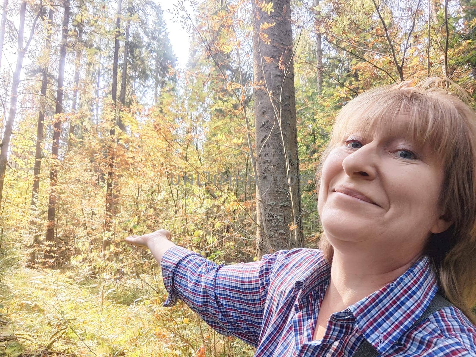 Blonde woman makes funny faces and points out scenery while exploring a colorful forest on her travel journey.