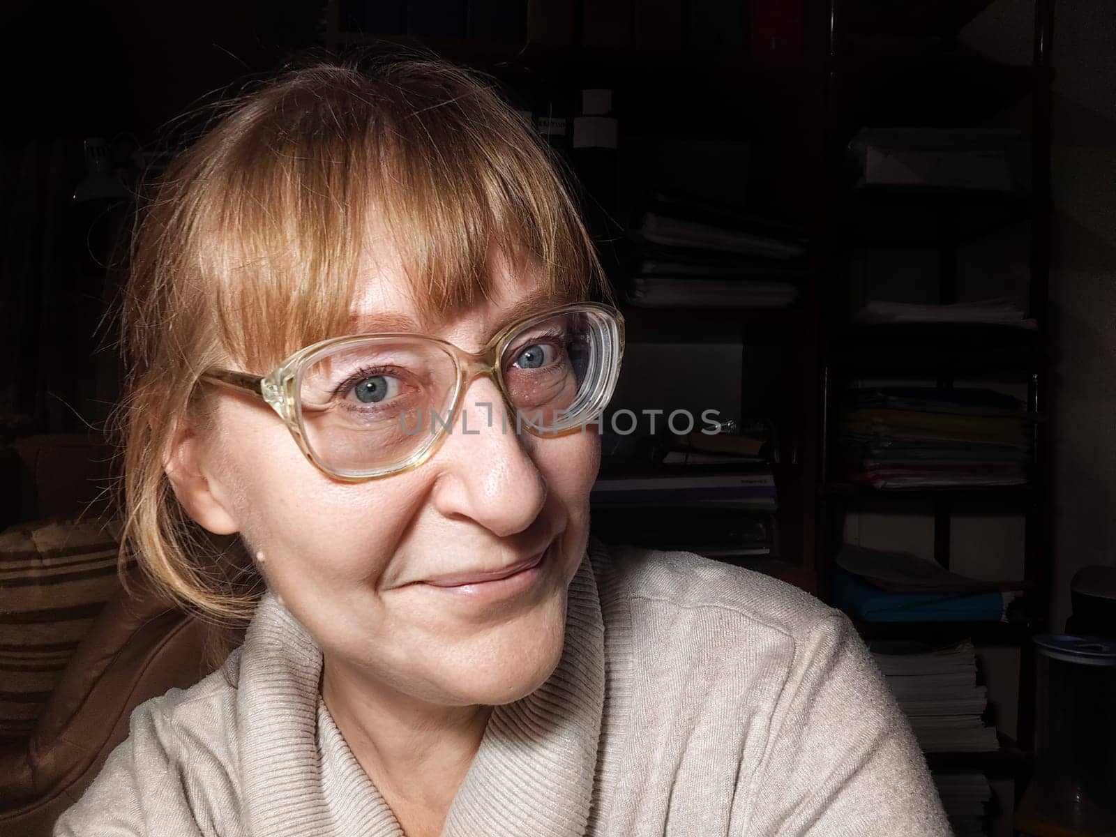 A mature woman with glasses takes a lighthearted selfie at home, capturing a moment of joy and creativity in her blogging journey.