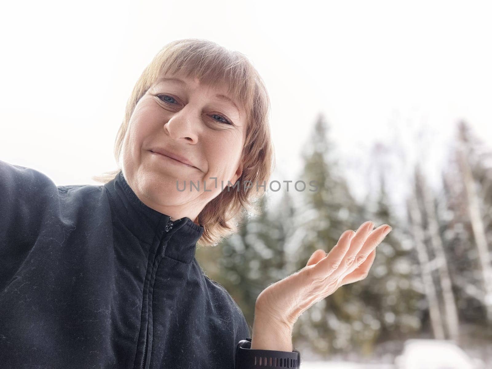 Middle-aged female blogger poses for a selfie amid snowy scenery, embracing her journey of exploration and travel.
