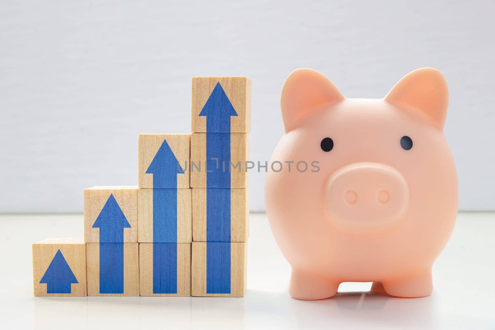 A piggy bank with wood blocks stacking as step stair with blue arrows up. Concept: Successful business, Business growth, Savings growth, Interest rate. Long term savings.