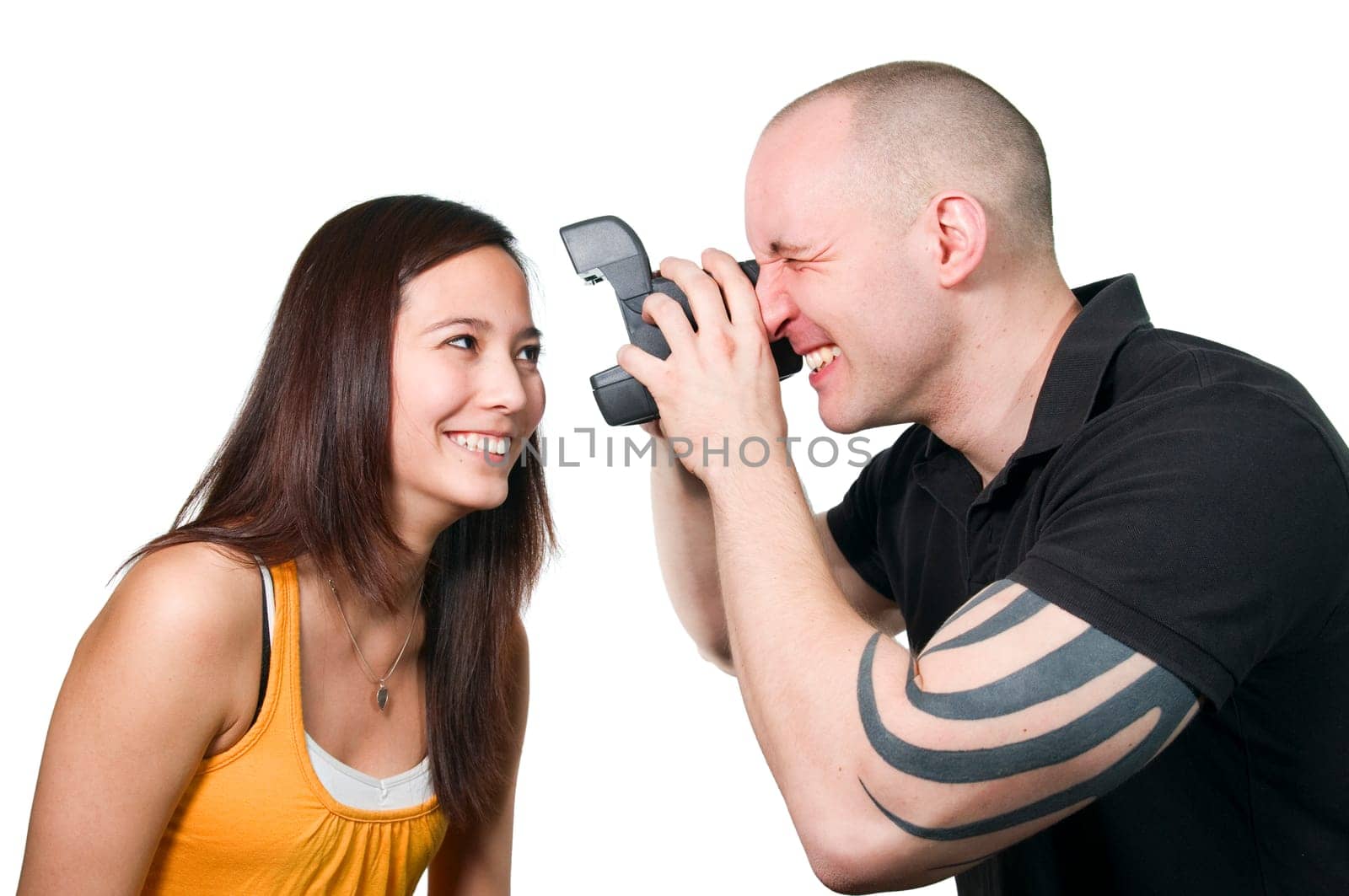 Upper body view of a young Asian woman very close in front of the camera of a young man with instant camera posing against white background.