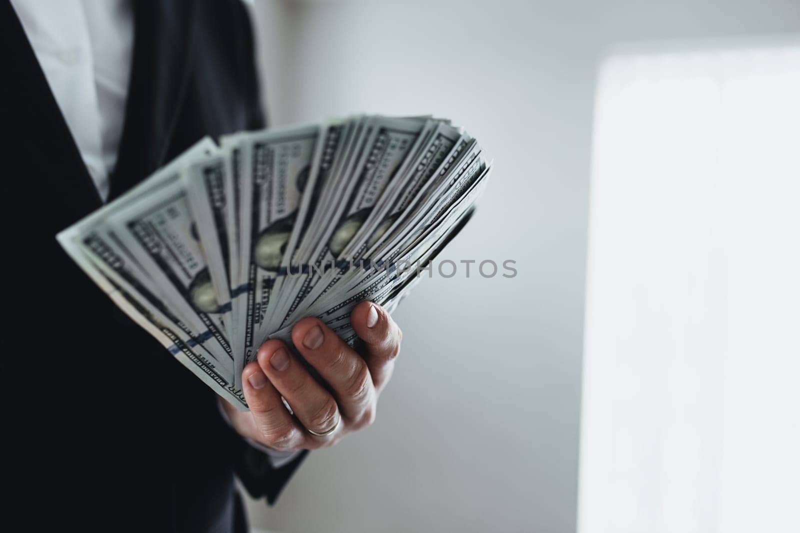 One hundred dollar bills money fun, in hand of man in suit and white shirt. Blurred background. High quality photo