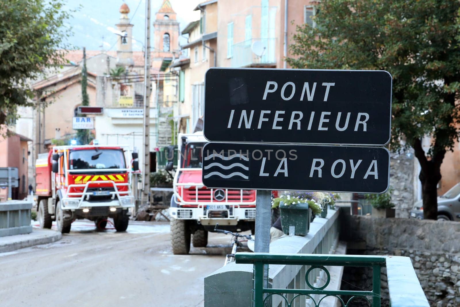 Breil-Sur-Roya, France - October 8, 2020: Roya River Sign With French Red Fire Trucks In Action In The Background In Breil-Sur-Roya, City Was Submerged By The Flooding Of The Roya River During Storm Alex