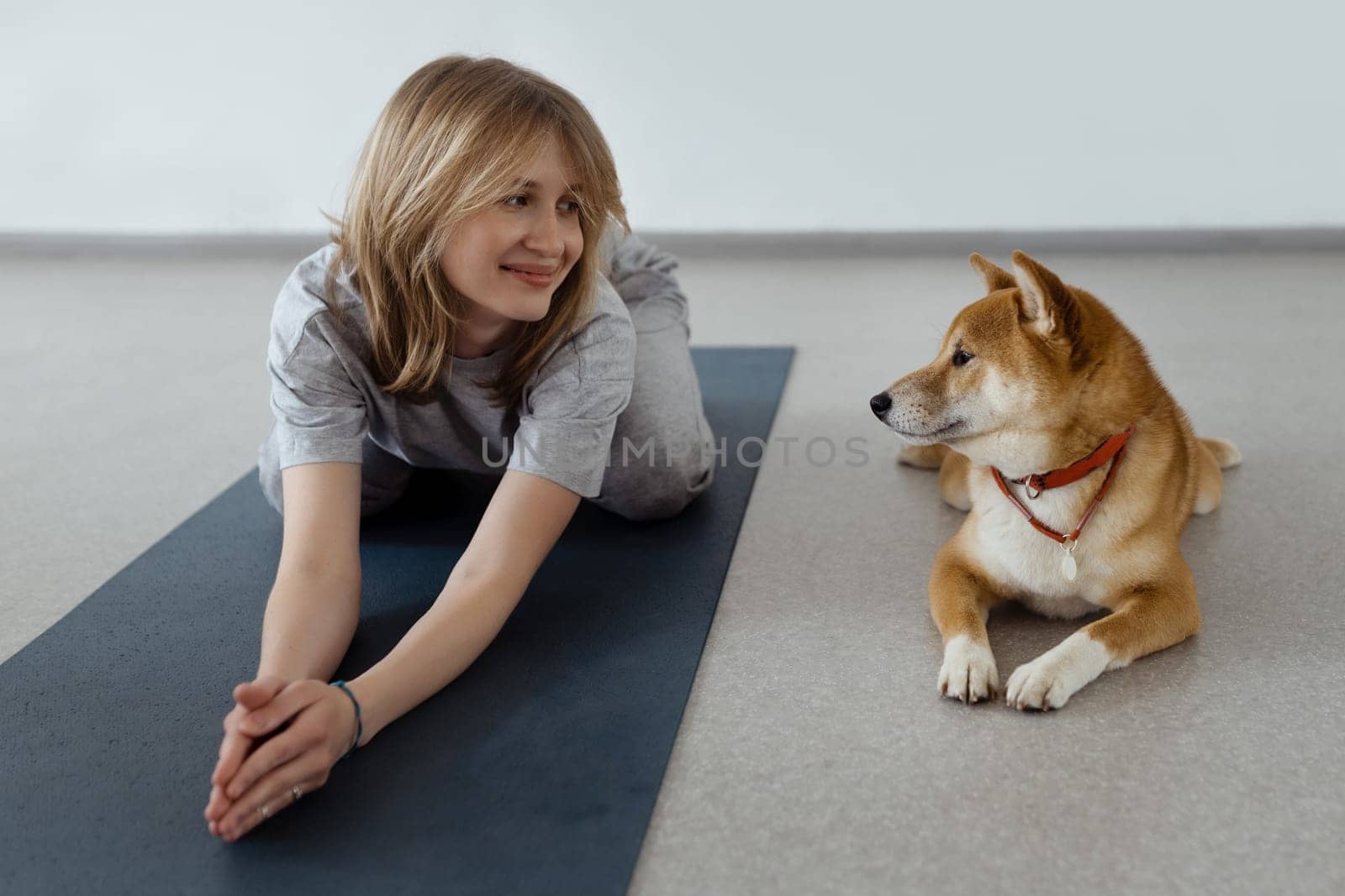 The dog practices yoga in the cobra pose in the studio. Young women meditating with pet.