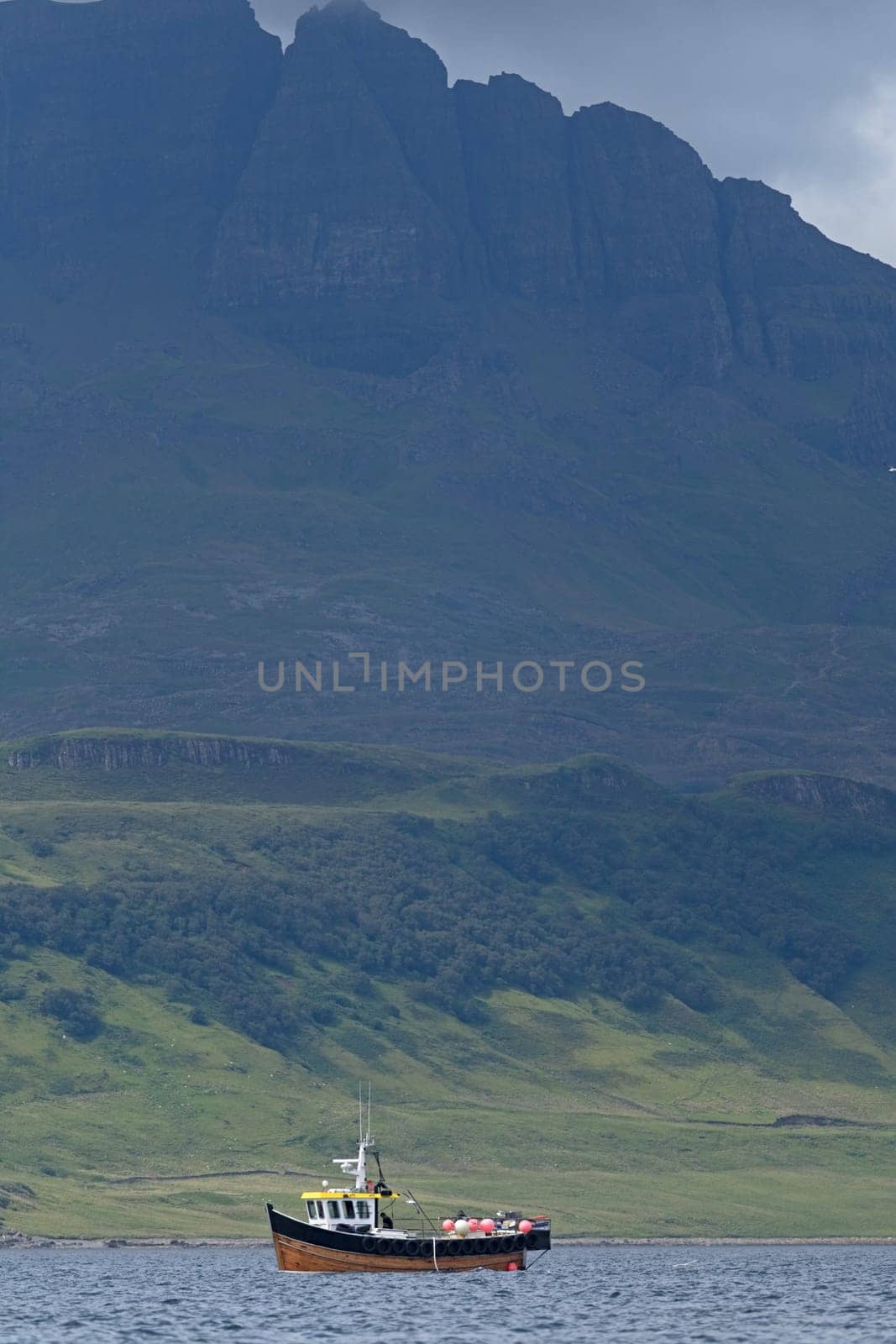 Rock formation named the old man of storr, on the isle of skye, looms imposingly over a small wooden fishing boat. Very dramatic scottish coastline.
