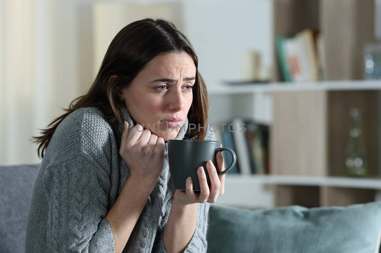 Ill woman getting cold drinking coffee complaining sittijng on a couch in winter at home