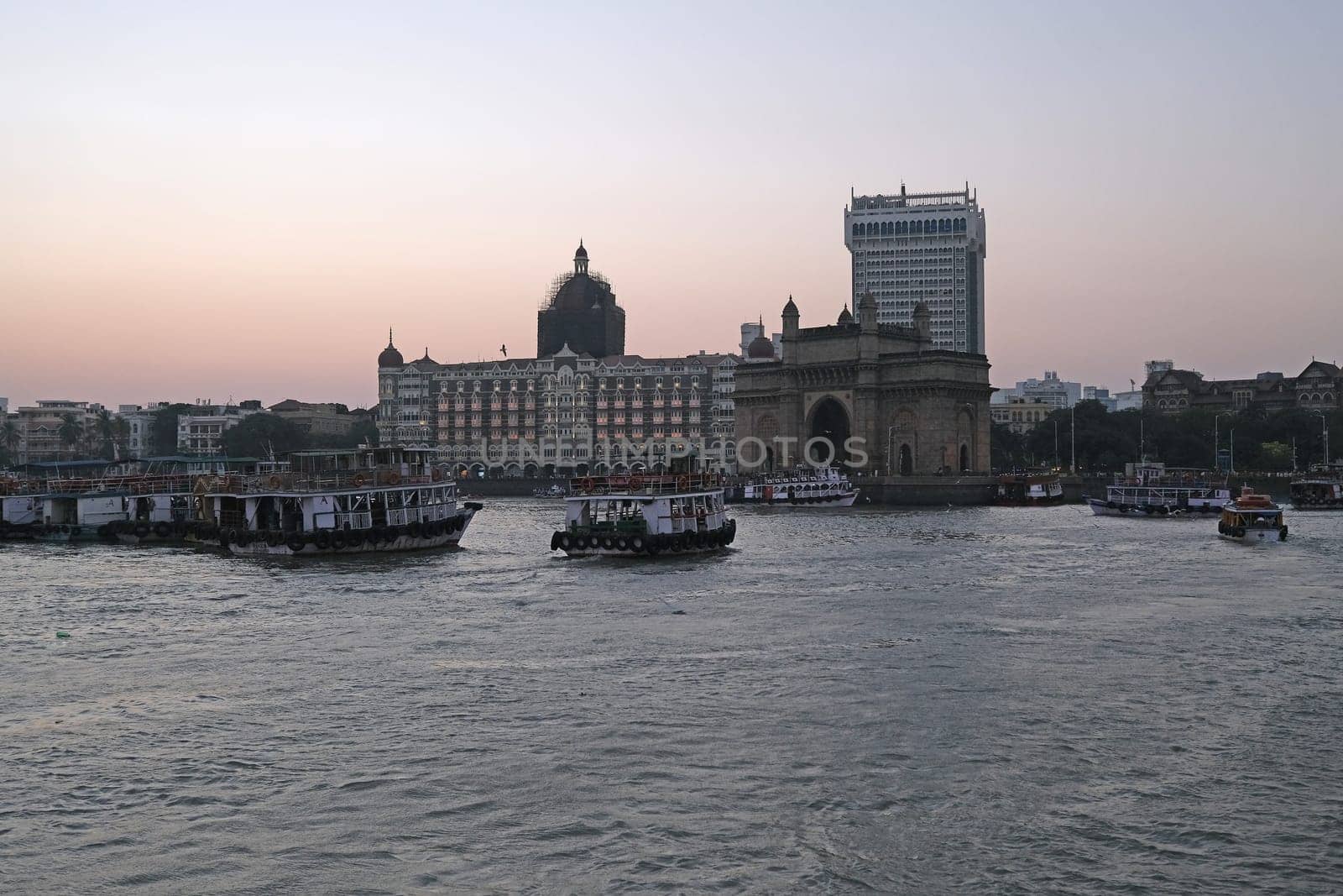 Taj Mahal hotel, Gateway of India and tourist boats in water of Arabian Sea on sunset in Mumbai, India
