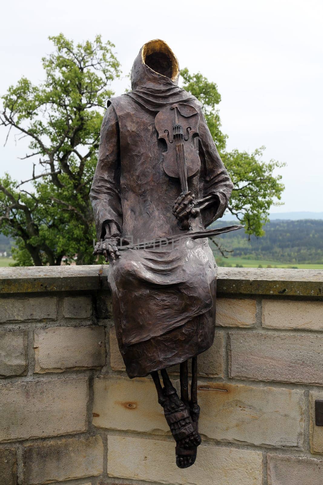 Monk Maurus with a violin sitting on the wall around the church in parish church of St. James in Hohenberg, Germany