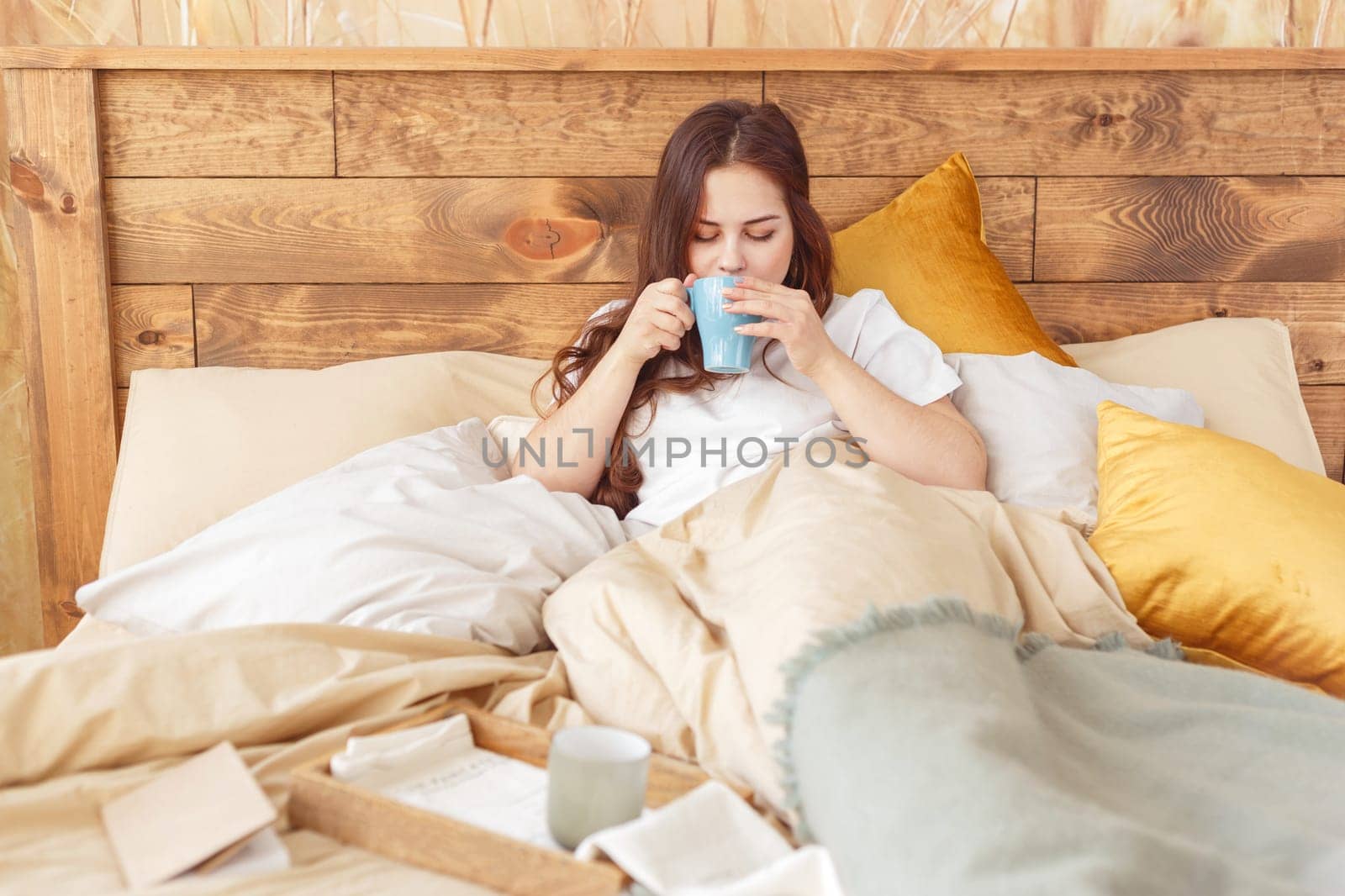 Young relaxing woman in bed in the morning with a mug of tea.