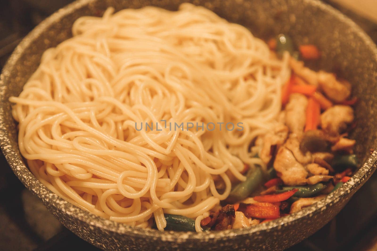 Fried noodles with vegetables and turkey meat in a black iron wok pan on