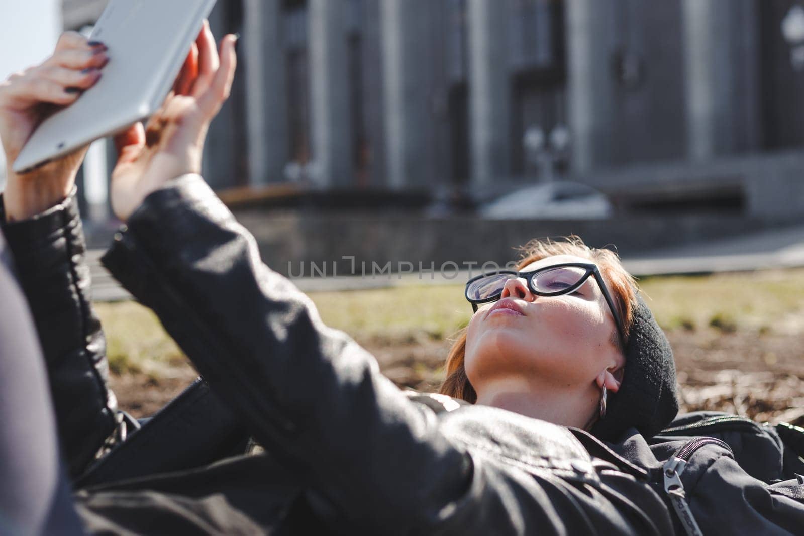 Young woman in glasses using tablet lying outdoor in the city.