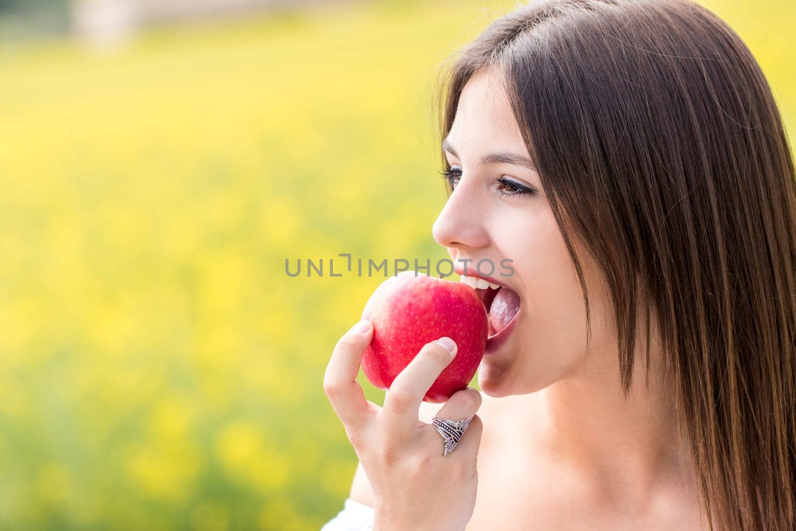 Close up face shot of Young woman biting red apple outdoors.