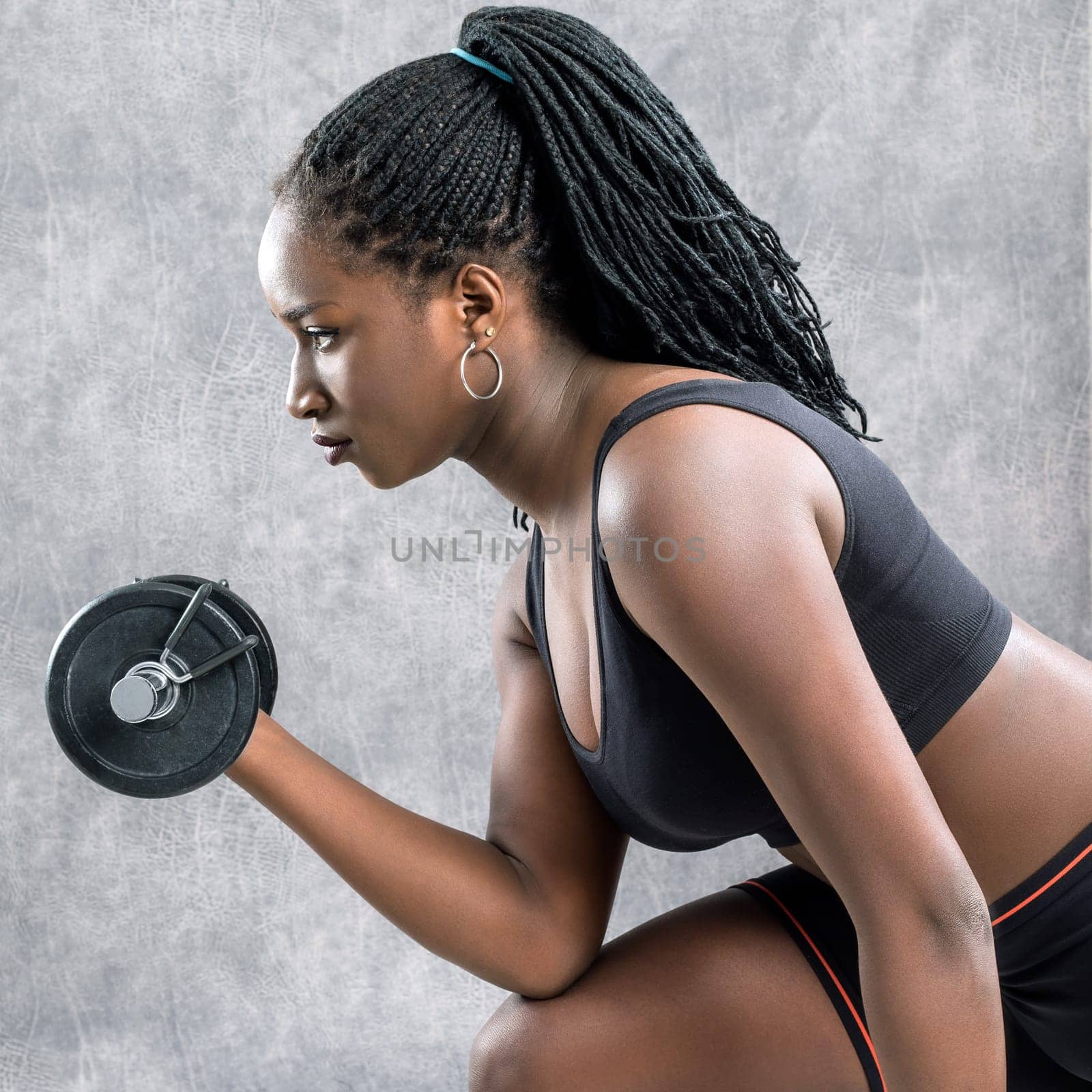 Close up portrait of african teen girl working out with dumbbell.Side view of young woman in sportswear against grey background.