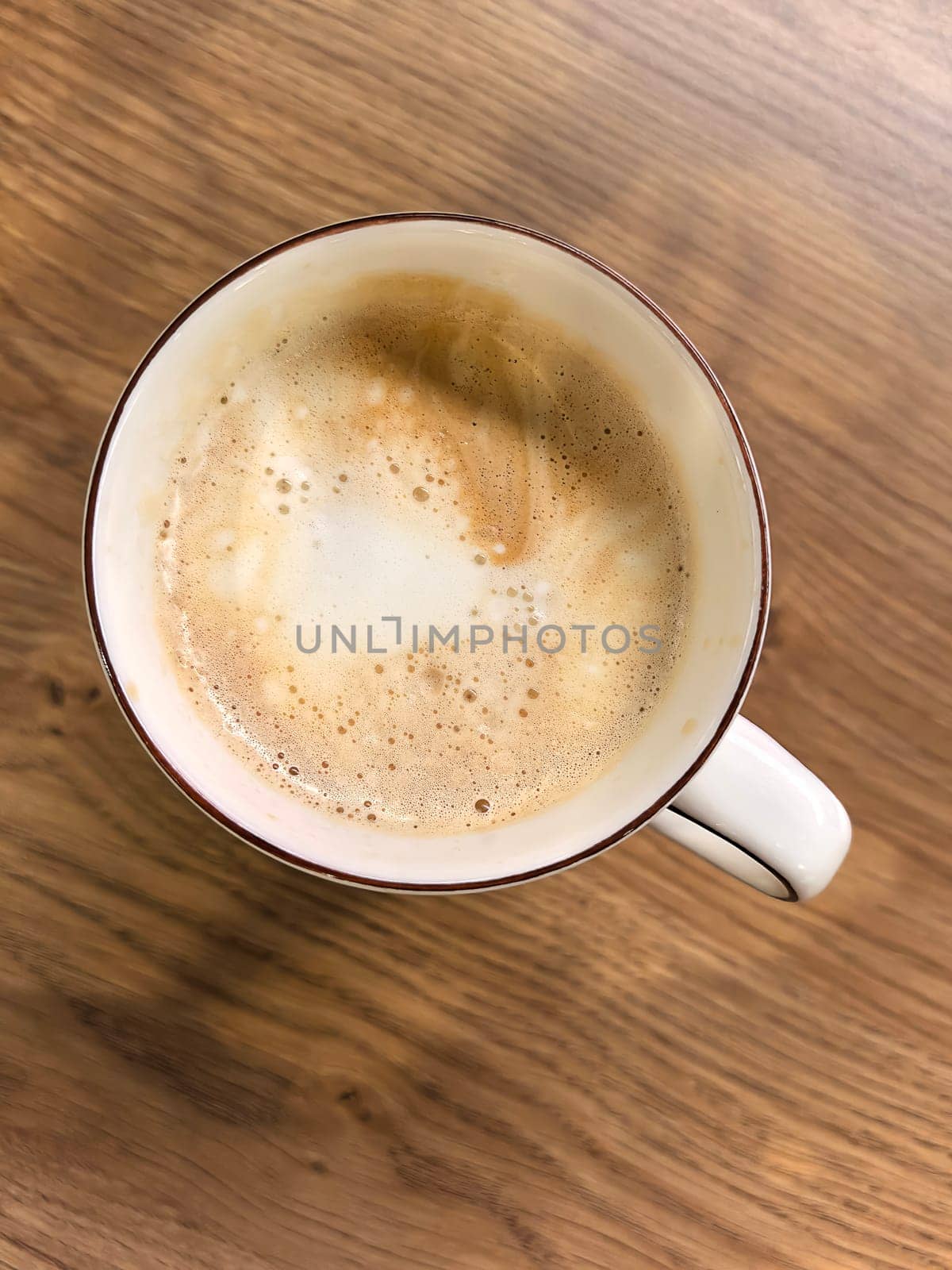 Cappuccino cup on wooden tabletop in coffee shop, top view. Coffee break in everyday life. Selective focus. Photo taken on mobile device.