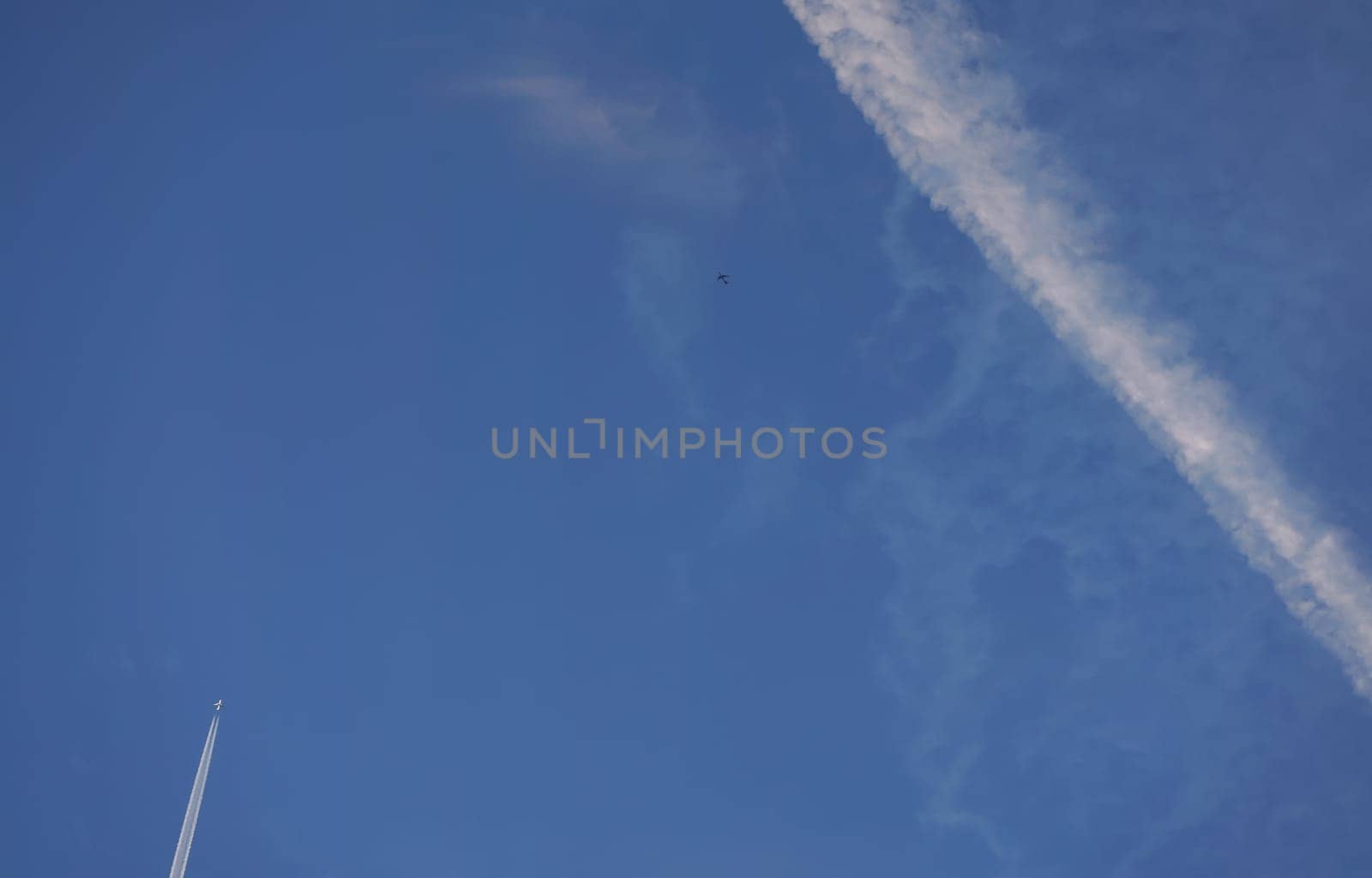 White trails from commercial airplanes, another plane flying, chemtrails conspiracy theory concept.