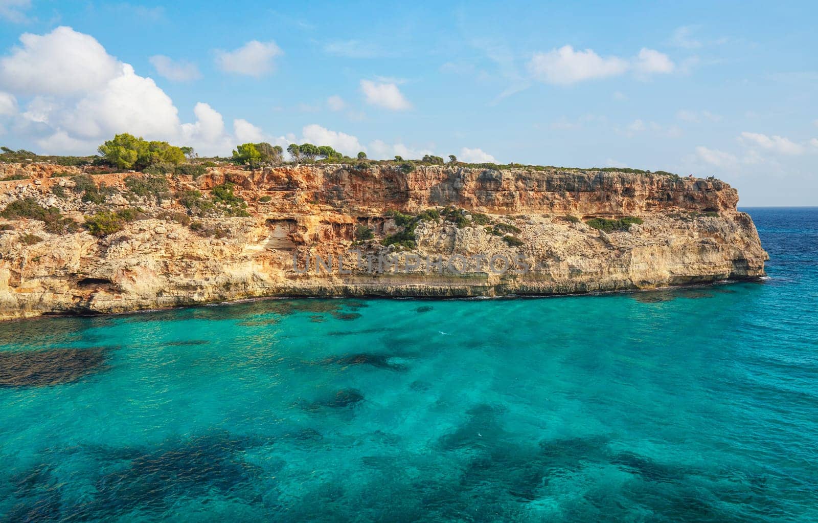 Clear blue green sea water, rocky cliffs around - nice sunny day at Ansa de s'Estri, Mallorca.