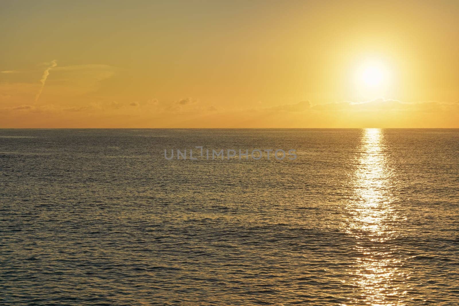 Sun rising above calm sea, clouds coloured to orange.
