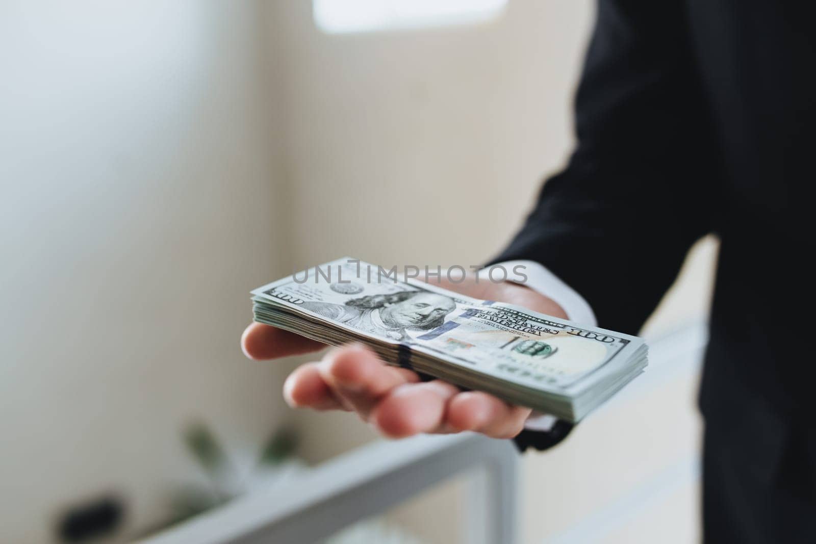 One hundred dollar bills money bundle, in hand of man in suit and white shirt. Blurred background. High quality photo