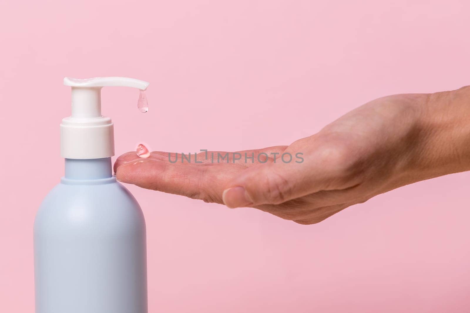 Female hand using alcohol gel sanitizer bottle dispenser, against coronavirus disease (Covid-19) . Antiseptic, Hygiene and Health concept. Minimalist style on pink background