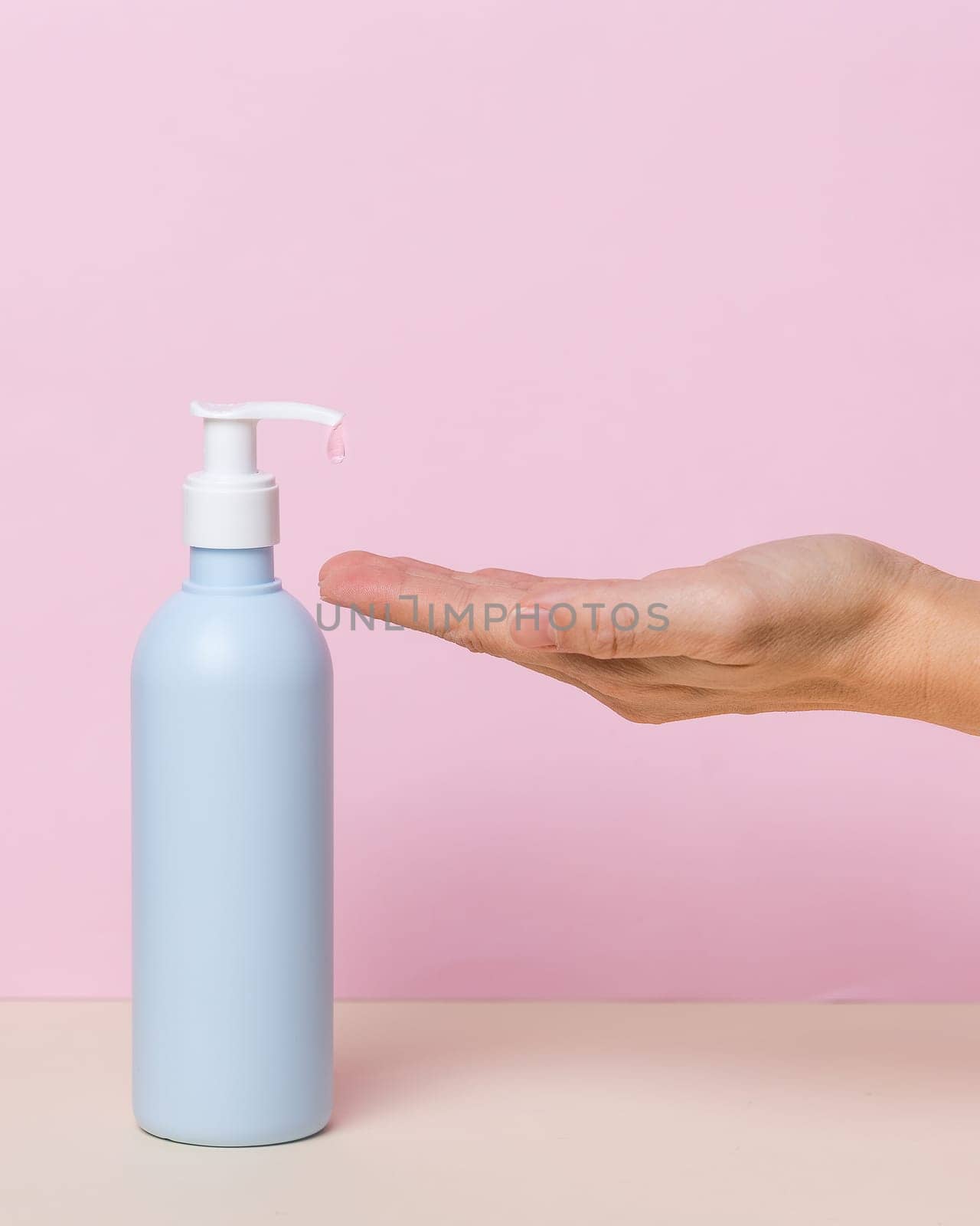 Female hand using alcohol gel sanitizer bottle dispenser, against coronavirus disease (Covid-19) . Antiseptic, Hygiene and Health concept. Minimalist style on pink background