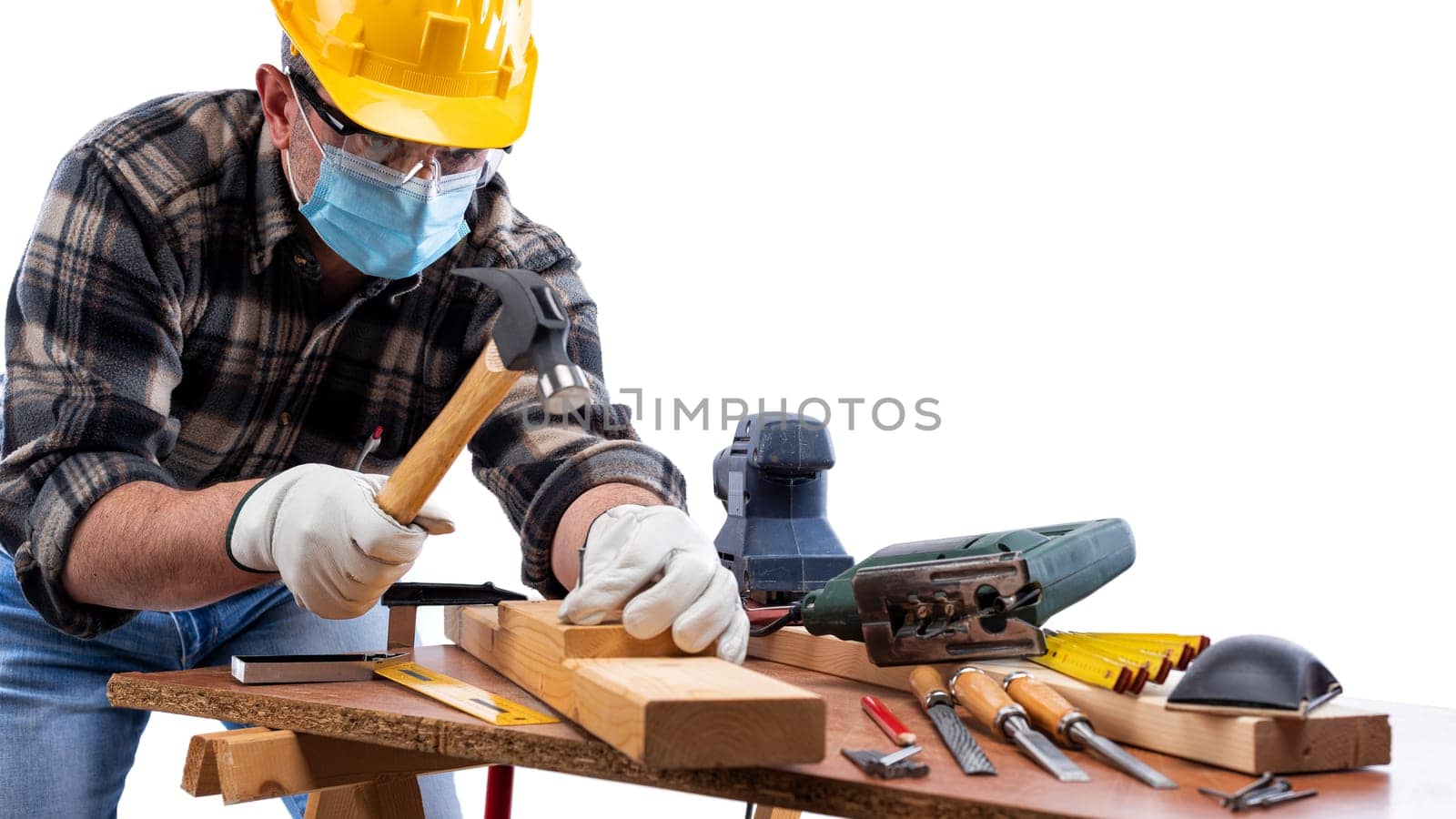 Carpenter worker at work isolated on white background, wears helmet, goggles, leather gloves and surgical mask to prevent coronavirus infection. Preventing Pandemic Covid-19 at the workplace.